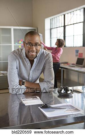 Businessman smiling at desk in office View Large Photo Image Stock Photo - Businessman smiling at desk in office. Fotosearch