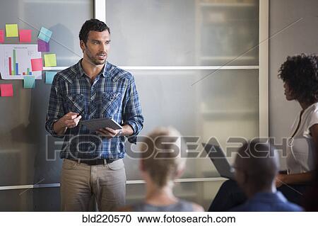 Stock Image - Businessman talking to colleagues in office meeting. Fotosearch