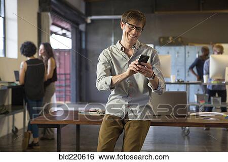 Stock Photograph - Businessman using cell phone in office. Fotosearch