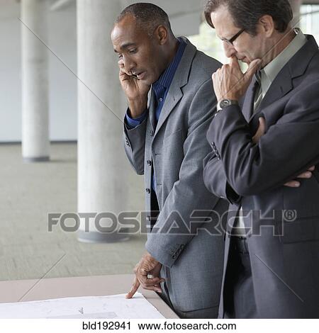 Stock Image - Businessmen looking at blueprints. Fotosearch