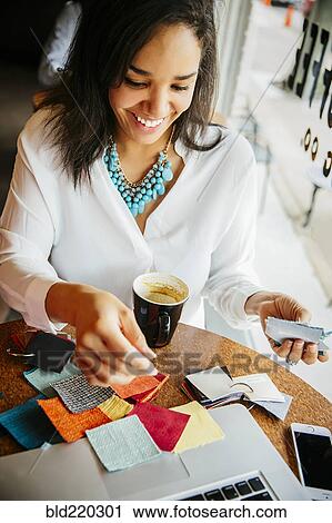 Stock Image - Businesswoman examining fabric samples in cafe. Fotosearch