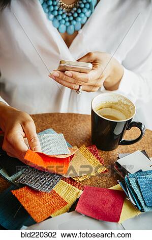 Stock Image - Businesswoman examining fabric samples in cafe. Fotosearch
