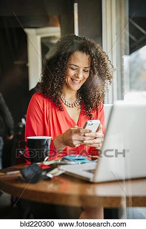 Stock Image - Businesswoman using cell phone in cafe. Fotosearch