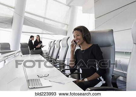 Stock Image - Businesswoman using cell phone in conference room. Fotosearch