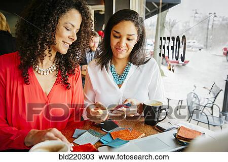 Stock Image - Businesswomen examining fabric samples in cafe. Fotosearch