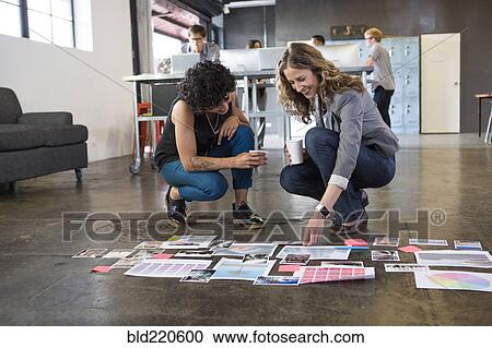 Stock Image - Businesswomen examining paperwork on office floor. Fotosearch