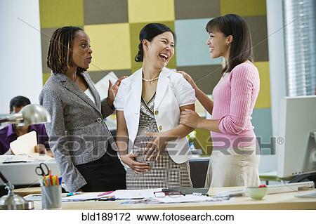 Stock Image - Businesswomen talking to pregnant co-worker. Fotosearch
