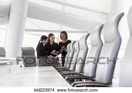 Picture - Businesswomen using cell phone in conference room. Fotosearch