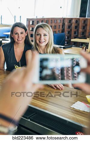 Stock Photograph - Caucasian bartender taking cell phone photograph of customers. Fotosearch