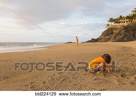 Stock Photo - Caucasian boy digging in sand on beach. Fotosearch