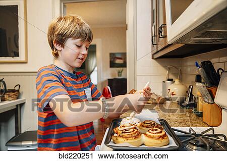 Caucasian boy frosting cinnamon rolls in kitchen View Large Photo Image Stock Image - Caucasian boy frosting cinnamon rolls in kitchen. Fotosearch