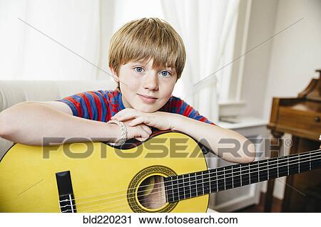 Stock Image - Caucasian boy holding guitar in living room. Fotosearch