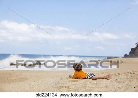 Picture - Caucasian boy laying on beach. Fotosearch