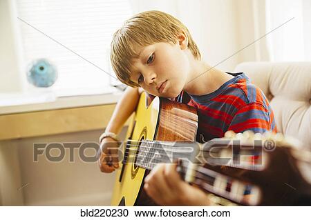 Stock Image - Caucasian boy playing guitar in living room. Fotosearch