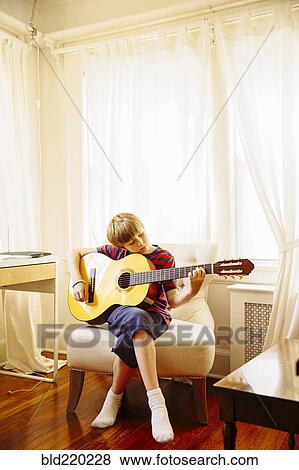 Stock Photo - Caucasian boy playing guitar in living room. Fotosearch