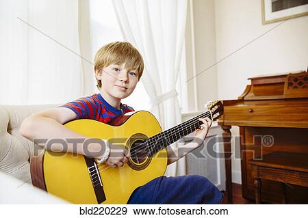 Stock Photo - Caucasian boy playing guitar in living room. Fotosearch