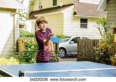 Stock Photograph - Caucasian boy playing table tennis in backyard. Fotosearch