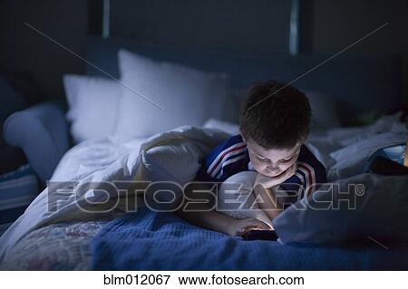 Caucasian boy playing video game in bed at night View Large Photo Image Stock Photo - Caucasian boy playing video game in bed at night. Fotosearch
