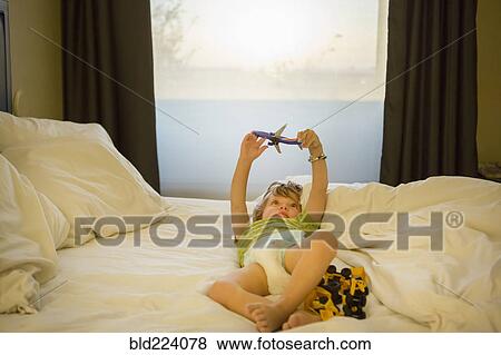Stock Photo - Caucasian boy playing with airplane on bed. Fotosearch