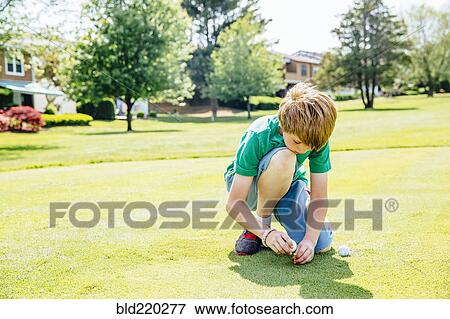Stock Photo - Caucasian boy setting up golf ball on course. Fotosearch