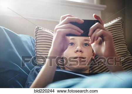 Caucasian boy using cell phone on bed View Large Photo Image Picture - Caucasian boy using cell phone on bed. Fotosearch
