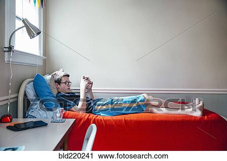 Stock Image - Caucasian boy using cell phone on bed. Fotosearch