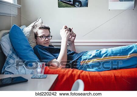 Stock Image - Caucasian boy using cell phone on bed. Fotosearch