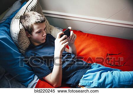 Caucasian boy using cell phone on bed View Large Photo Image Stock Photography - Caucasian boy using cell phone on bed. Fotosearch