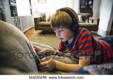 Stock Photograph - Caucasian boy using digital tablet on sofa. Fotosearch