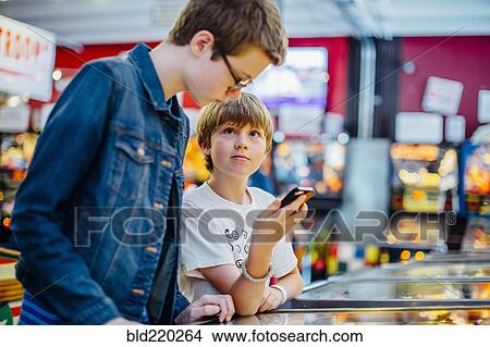 Picture - Caucasian brothers using cell phone in arcade. Fotosearch