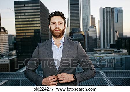 Stock Photo - Caucasian businessman buttoning jacket on urban rooftop. Fotosearch