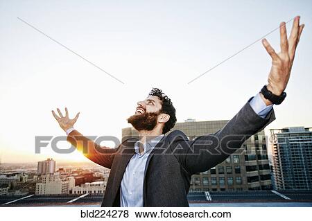 Stock Photo - Caucasian businessman celebrating on urban rooftop. Fotosearch