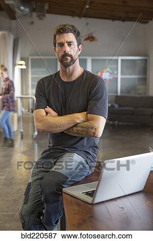 Stock Photo - Caucasian businessman sitting on desk with laptop. Fotosearch