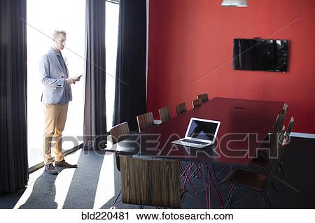 Stock Image - Caucasian businessman talking on cell phone in conference room. Fotosearch