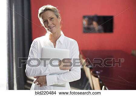 Picture - Caucasian businesswoman carrying laptop in conference room. Fotosearch