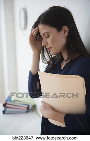 Stock Photo - Caucasian businesswoman with headache holding file folder in office. Fotosearch