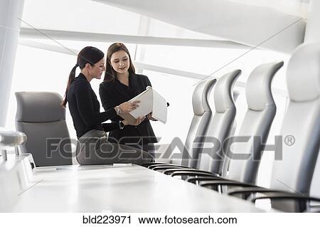 Stock Image - Caucasian businesswomen at conference table reading notepad. Fotosearch