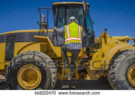 Stock Image - Caucasian construction worker climbing onto earth mover. Fotosearch