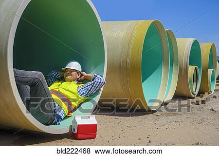 Stock Photo - Caucasian construction worker napping inside large pipe. Fotosearch