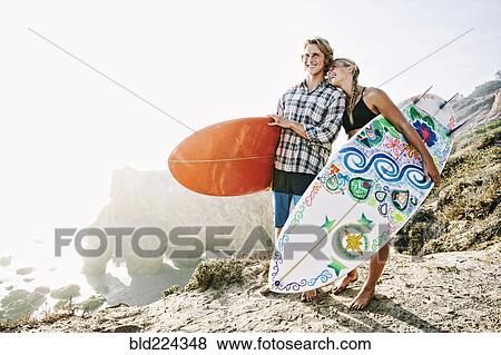 Stock Photo - Caucasian couple carrying surfboards at beach. Fotosearch
