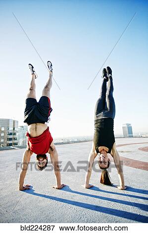 Stock Photo - Caucasian couple doing handstands on urban rooftop. Fotosearch