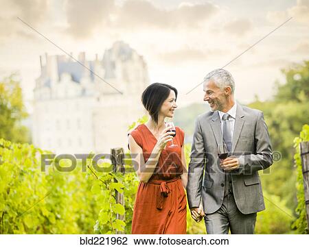 Stock Image - Caucasian couple enjoying wine in vineyard. Fotosearch