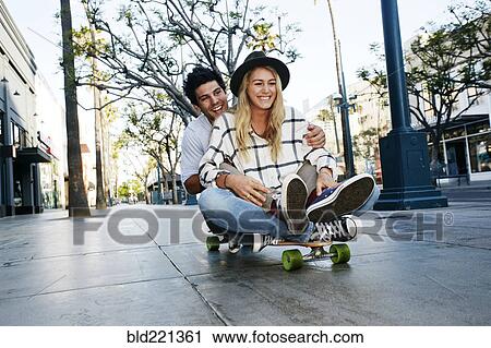 Stock Image - Caucasian couple riding skateboard. Fotosearch