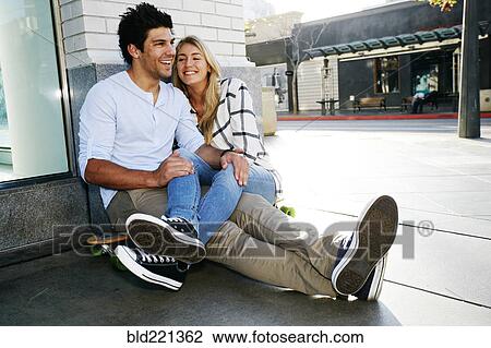 Stock Image - Caucasian couple sitting on sidewalk. Fotosearch