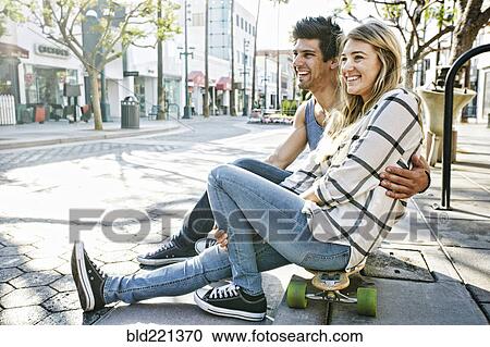 Stock Image - Caucasian couple sitting on skateboards. Fotosearch