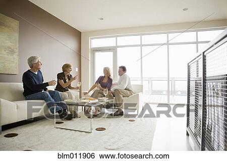 Stock Photograph - Caucasian couples drinking wine in modern living room. Fotosearch
