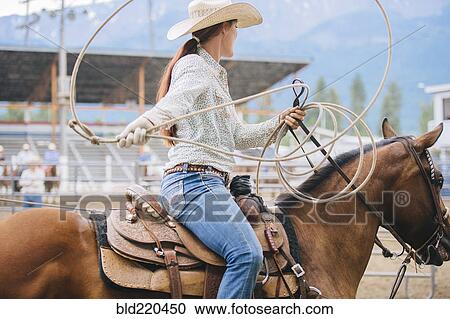 Stock Image - Caucasian cowgirl twirling lasso in rodeo. Fotosearch