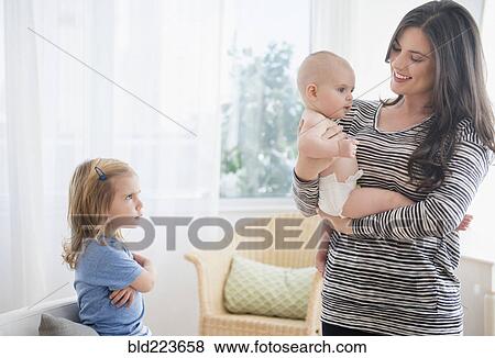 Stock Photo - Caucasian daughter jealous of mother holding baby sister. Fotosearch