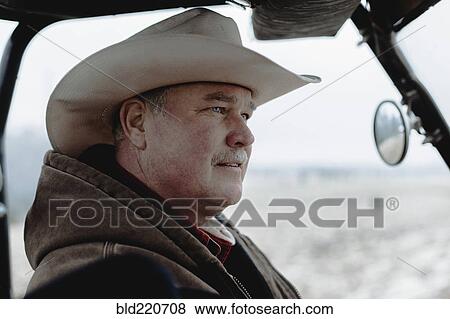 Stock Photo - Caucasian farmer driving equipment in farm field. Fotosearch
