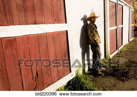 Stock Photograph - Caucasian farmer leaning on barn wall. Fotosearch